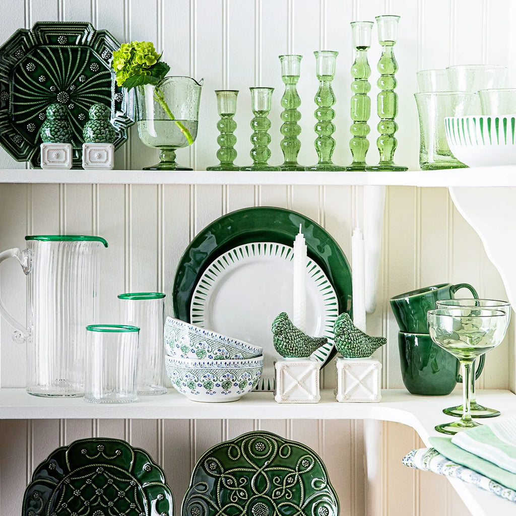 Puro mug in basil green, displayed among various green glassware and ceramics on a white shelf.