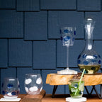 Drop white stemless wine glass with blue and white polka dots, displayed on a wooden stand against a dark textured backgro...