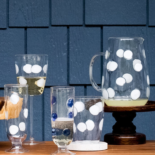 Drop blue tall tumbler with white polka dots, displayed alongside a matching pitcher and other glassware on a wooden surface.