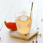 Drop white tall tumbler with a light beverage, ice, and a garnish on a marble coaster beside an orange slice.