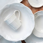 Giorno white mug with a textured design, placed on a white plate among other tabletop items.