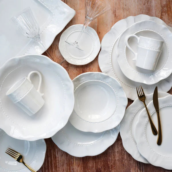 Giorno white mug with a textured rim, placed among various white tabletop dishes on a wooden surface.