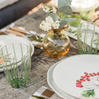 Nuovo Stripe green tall tumbler with vertical stripes, placed on a rustic wooden table alongside plates and a small vase.