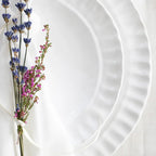 Pietra Serena dinner plate in white, featuring a textured rim, accompanied by dried lavender and pink flowers.