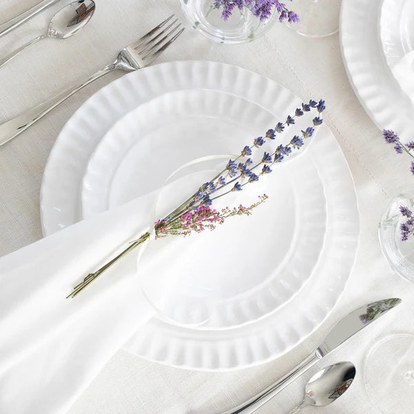 Pietra Serena dinner plate in white with a ribbed edge, set on a table with silver cutlery and lavender sprigs.
