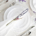Pietra Serena dinner plate in white with a ribbed edge, set on a table with silver cutlery and lavender sprigs.