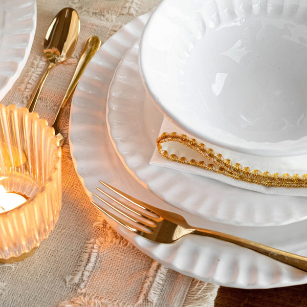 Pietra Serena salad plate in white with a textured rim, displayed with gold utensils and a candle on a textured tablecloth.
