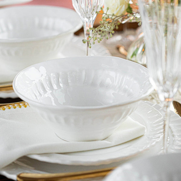 Pietra Serena cereal bowl in white, featuring a textured rim, placed on a table setting with elegant glassware and flowers.