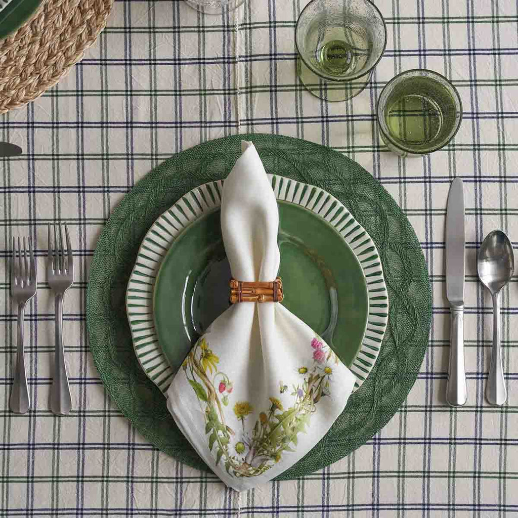 Sitio stripe dinner plate in basil color, set on a green placemat with a floral napkin and glassware.