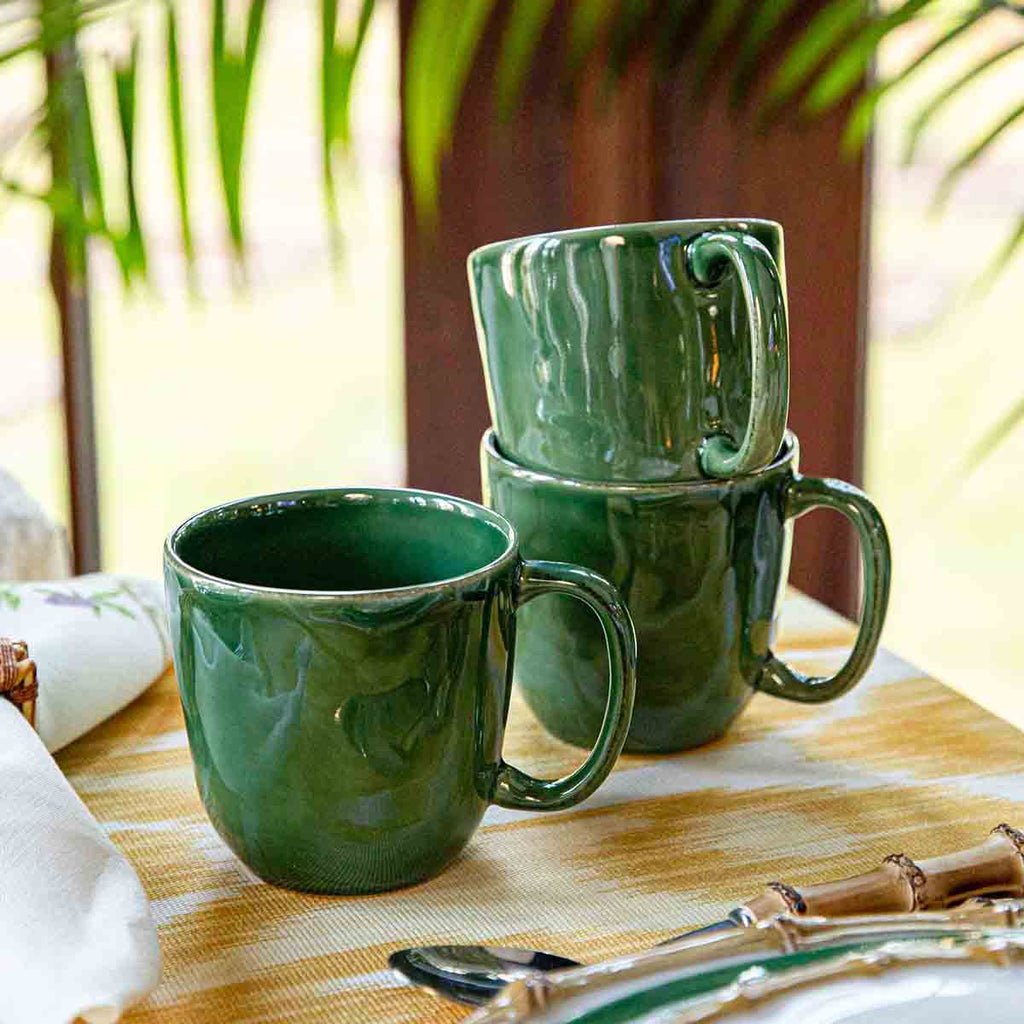 Puro mug in basil green stacked on a table with a yellow tablecloth and cutlery in the background.