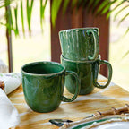 Puro mug in basil green stacked on a table with a yellow tablecloth and cutlery in the background.