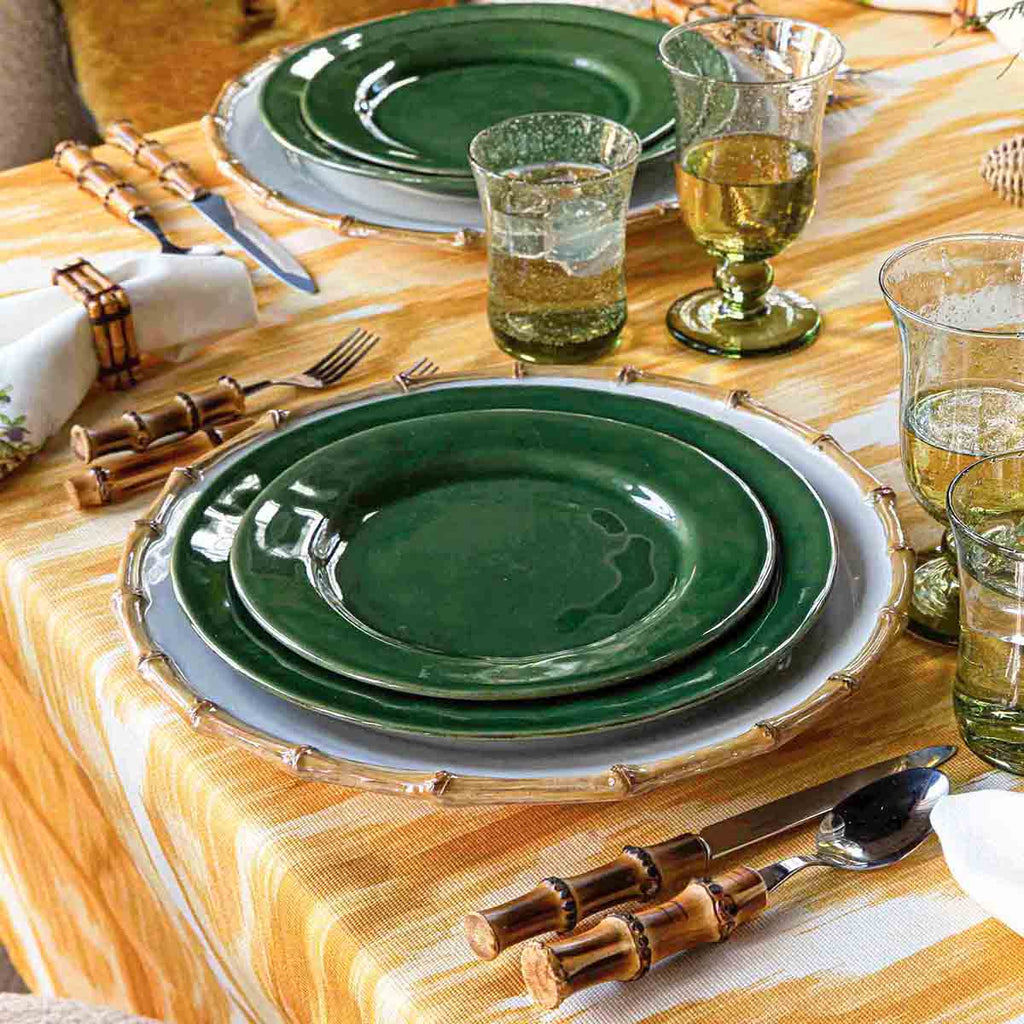 Puro dinner plate in basil green, set on a table with bamboo utensils and glassware, surrounded by a yellow tablecloth.