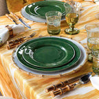 Puro dinner plate in basil green, set on a table with bamboo utensils and glassware, surrounded by a yellow tablecloth.
