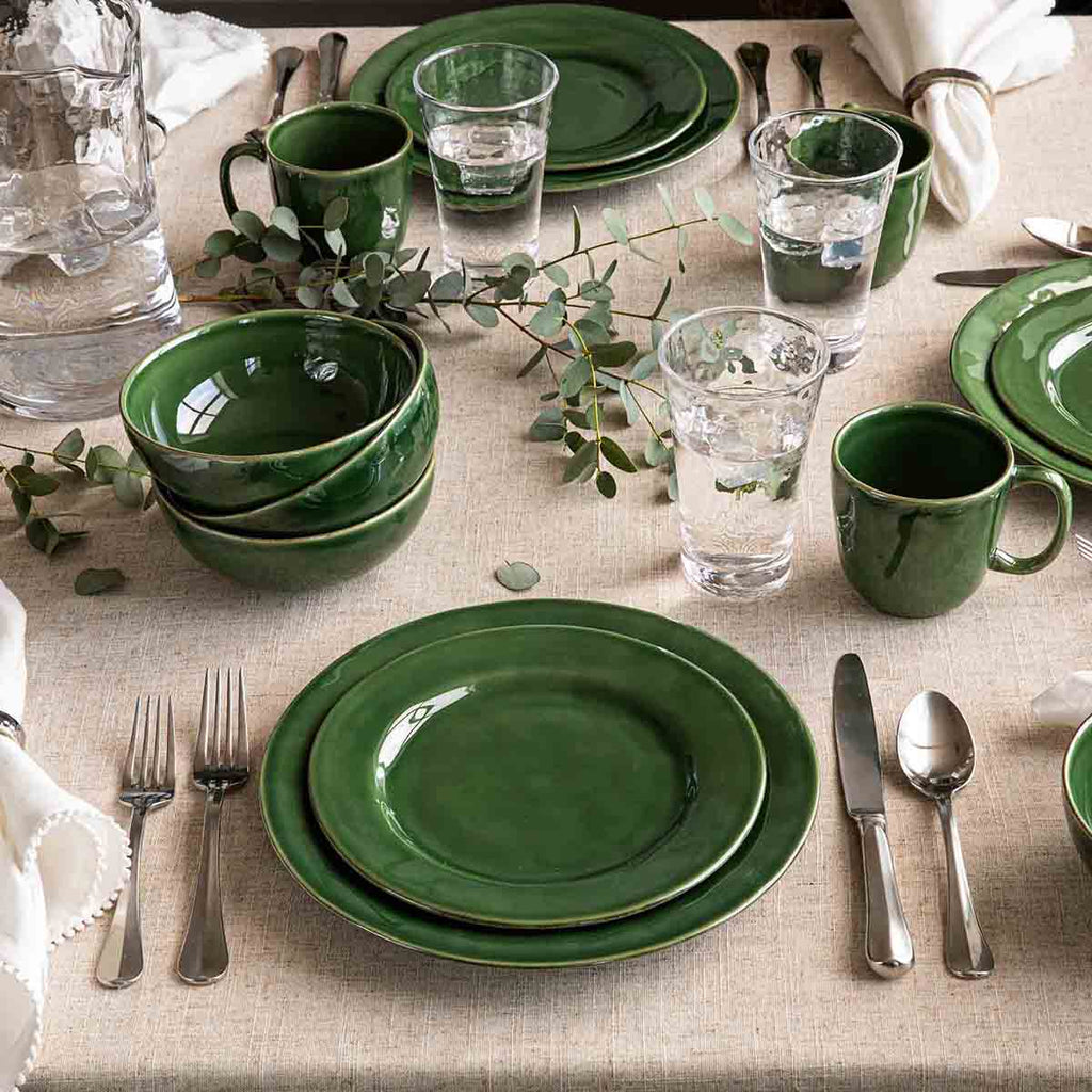 Puro dessert/salad plate in basil green, displayed among matching tableware on a beige tablecloth.