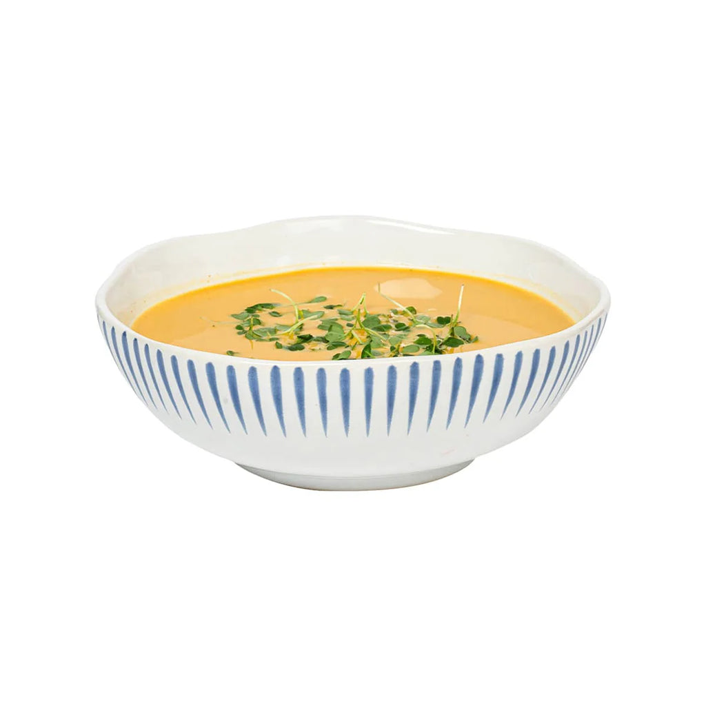 Sitio stripe coupe bowl in Delft blue with white stripes, filled with orange soup and garnished with herbs.